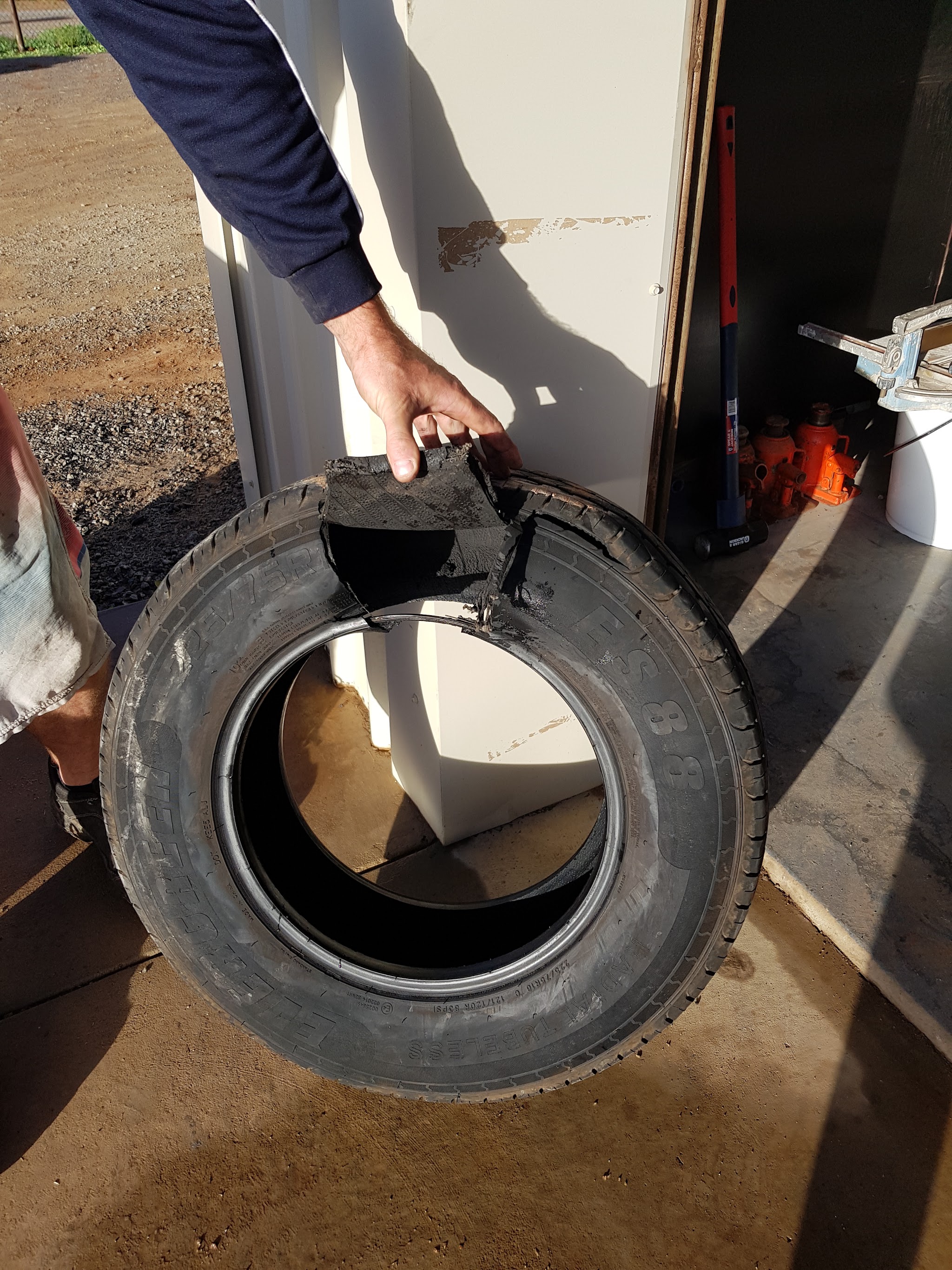 A delaminated truck tyre held open at the workshop, the tread peeled away from the carcass