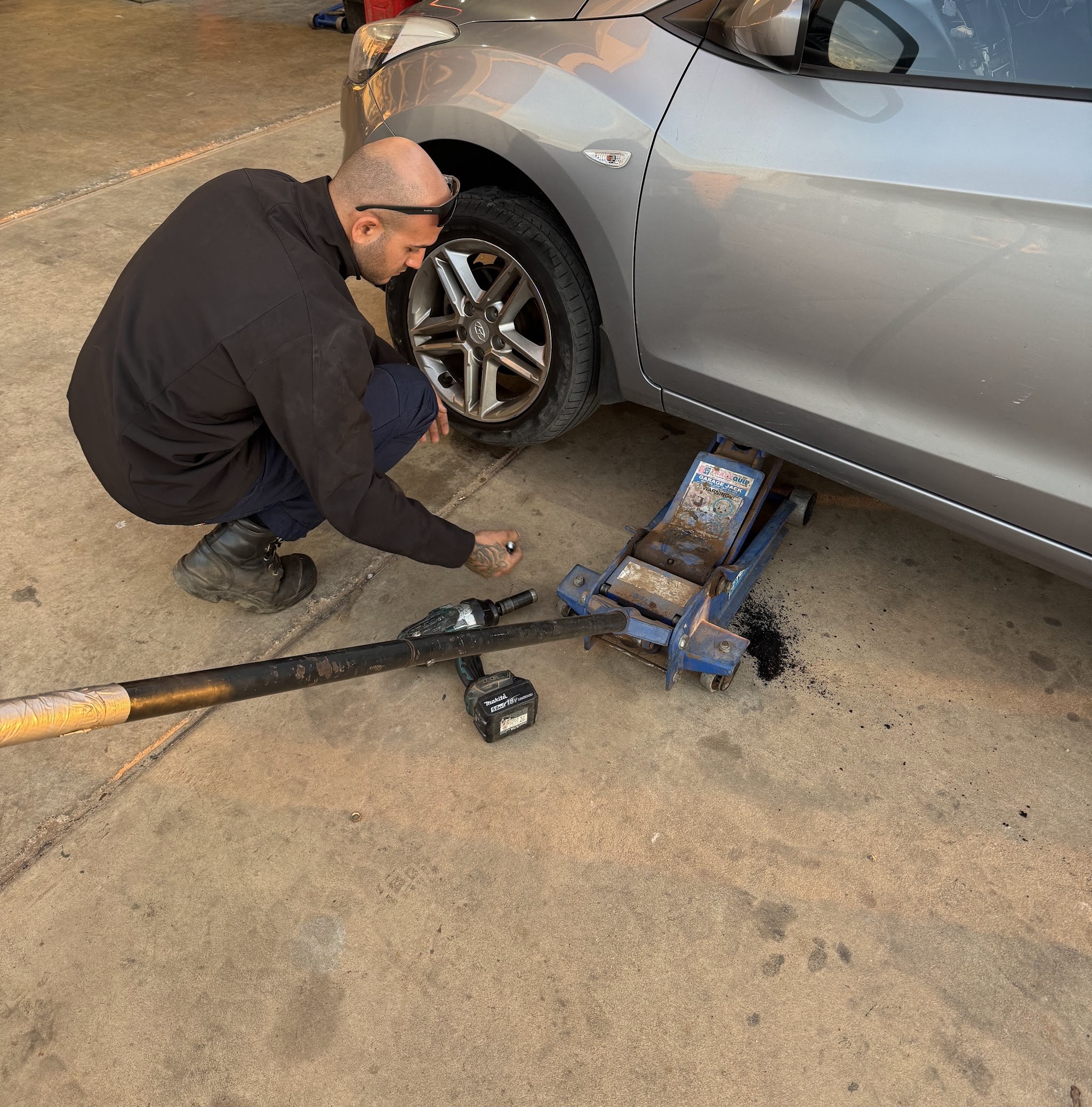 A fitter working on the front wheel of a car raised on a trolley jack inside the workshop